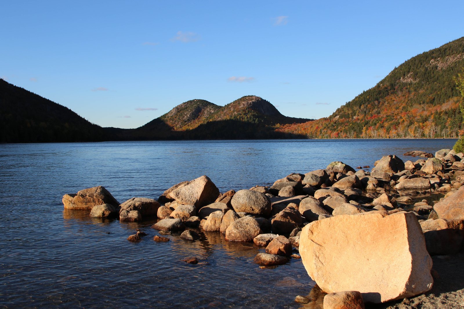 Jordan Pond seen from its rocky shore, with the two rounded hills known as the Bubbles rising beyond the far end of the water, autumn colour on their slopes
