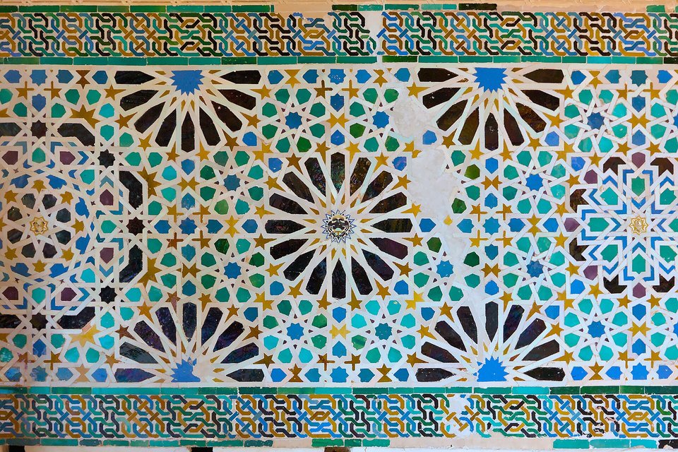 A wall of glazed tile mosaic in blue, green, ochre and black forming interlocking stars and polygons within a border