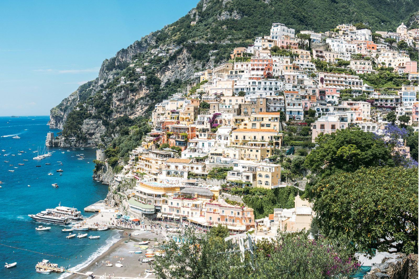 A colourful town of houses stacked steeply down a hillside to a bay of blue water under a clear sky