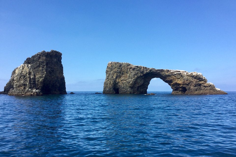 A natural rock arch and a tall stack standing in calm blue water under a clear sky