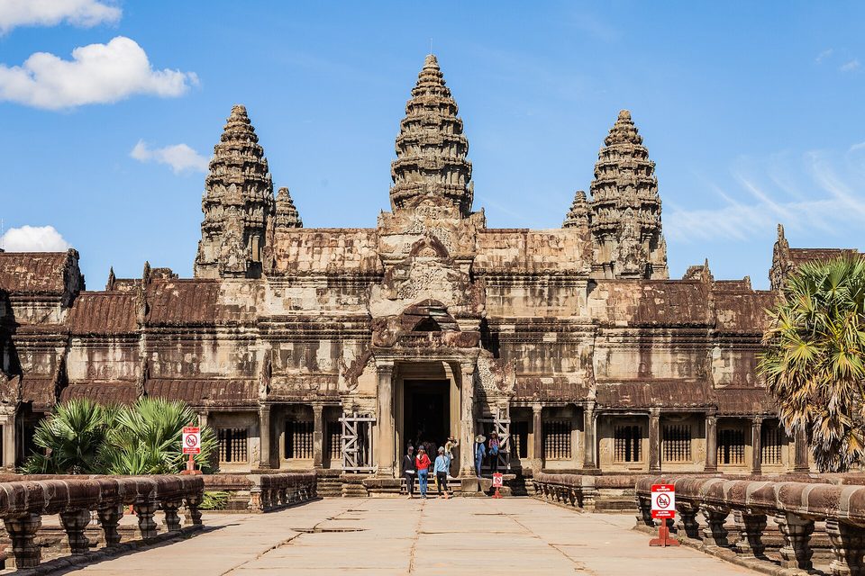 A temple front with three tiered towers of grey sandstone beyond a paved causeway and stone railings under a blue sky