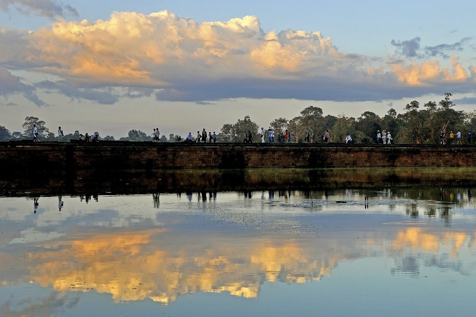 A long wall and the temple beyond reflected in a broad moat under a sky of yellow-lit clouds