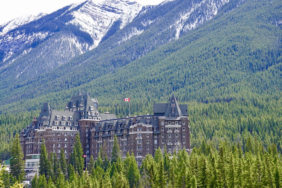 A large stone and turreted hotel among dark conifers at the foot of a snow-dusted mountain slope