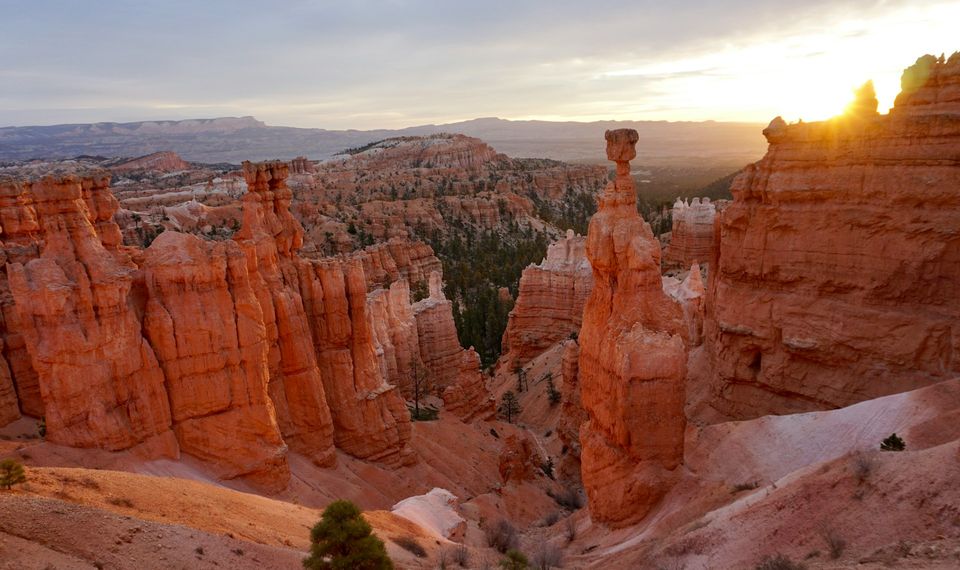 A tall rock spire silhouetted against a bright sunrise with the amphitheatre glowing beyond