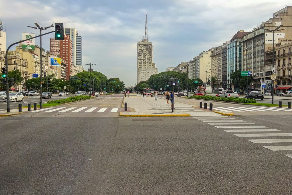 A very wide city avenue with crossings and central islands between tall buildings