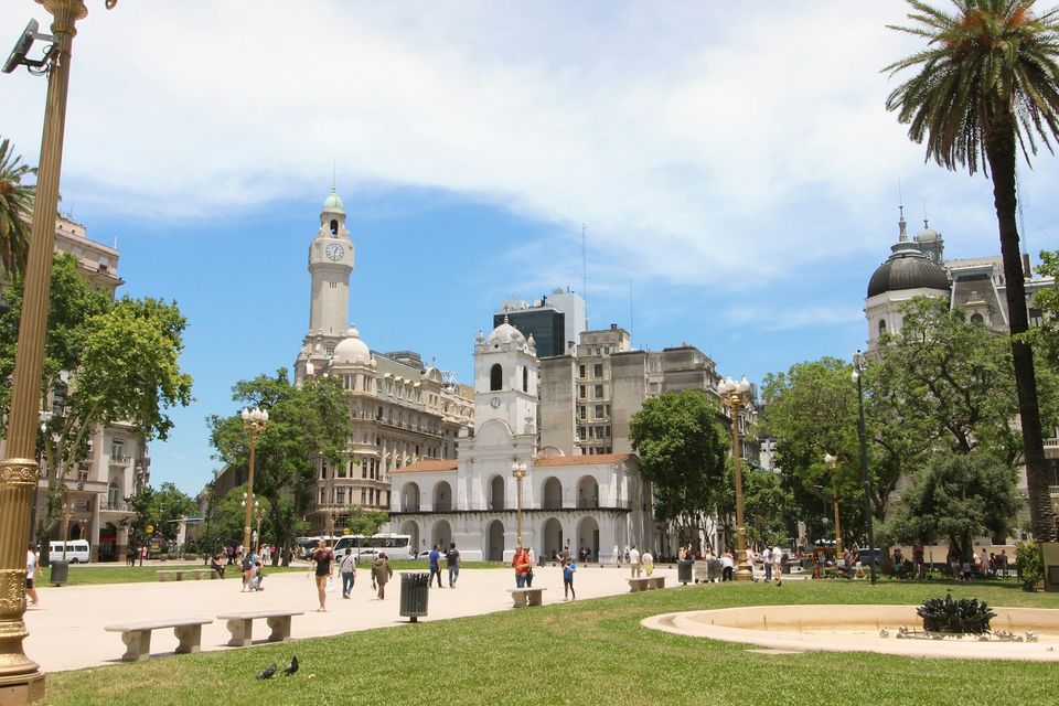 A white colonial arcaded town hall with a clock tower across a square under a clear sky