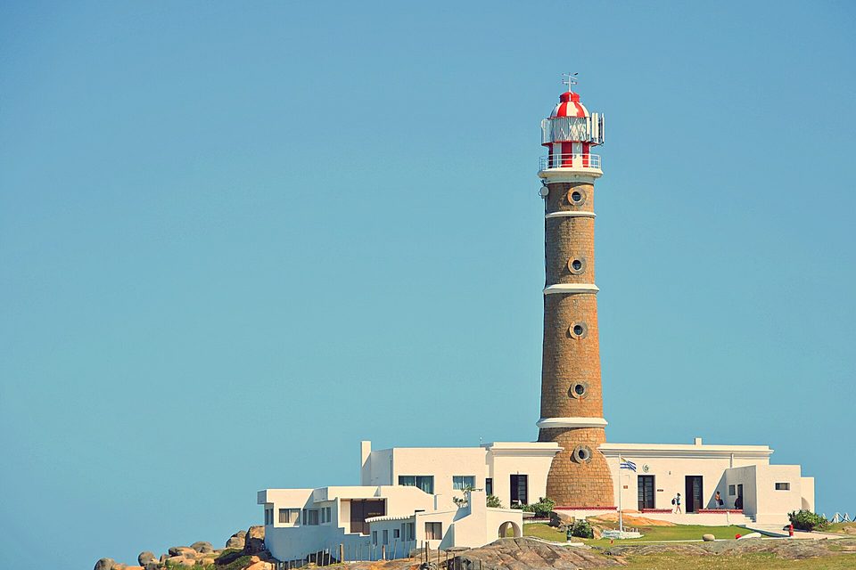 A stone lighthouse tower above white keepers' buildings under a deep blue sky