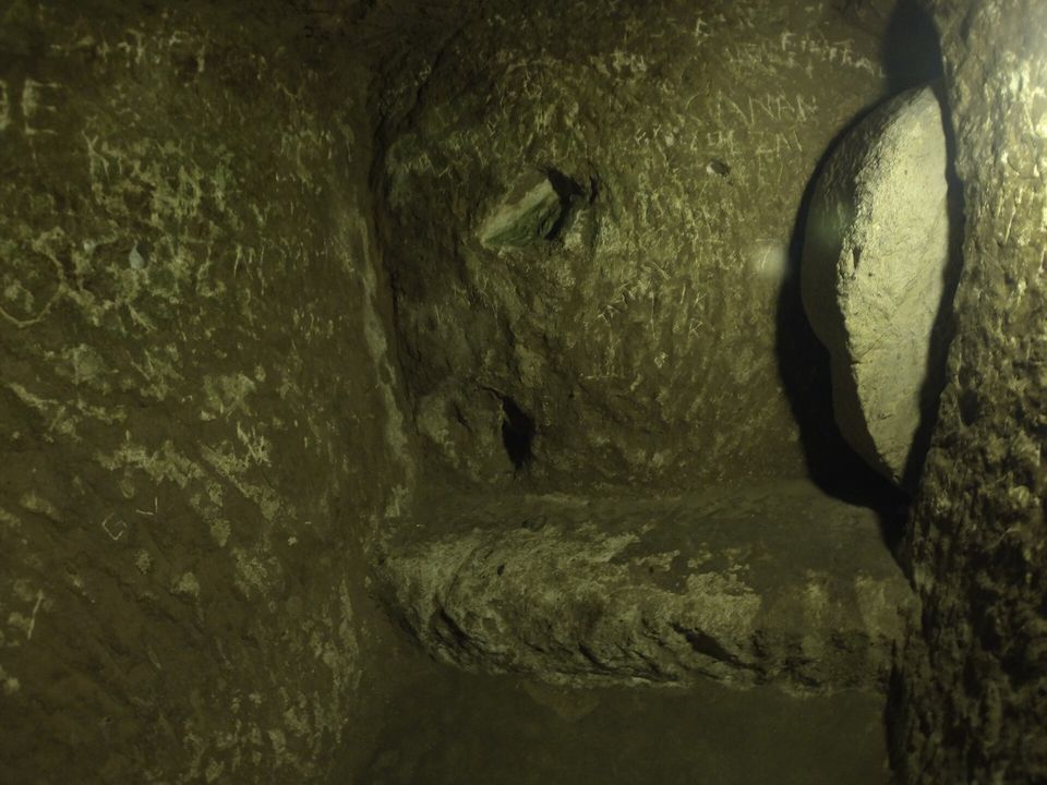 A round stone door seen edge-on beside a dim, scratched rock passage