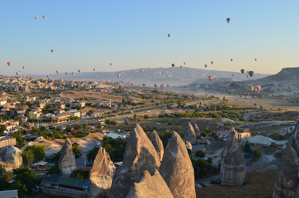 Dozens of hot-air balloons over rock valleys in early light