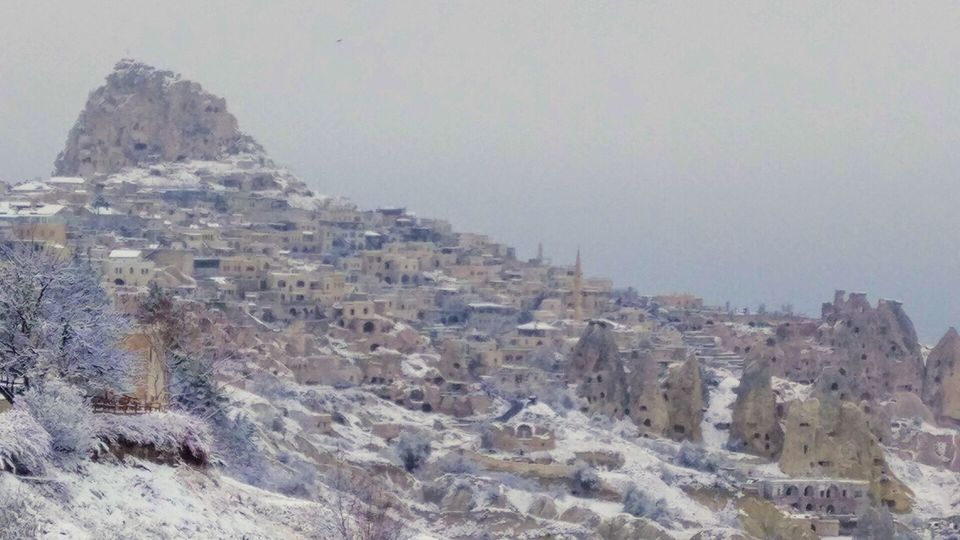 A tall honeycombed rock citadel above a snowy village