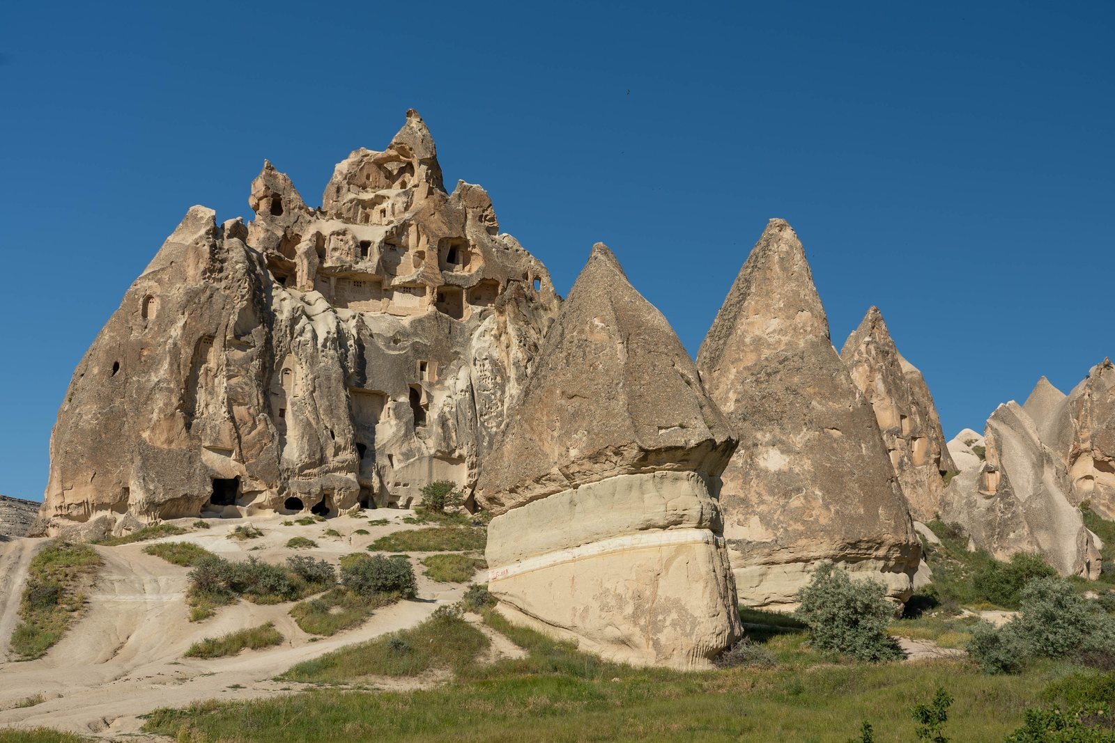 A pale volcanic tuff cone cut with rows of windows and doorways into rooms hollowed from the rock, pointed fairy chimneys around it