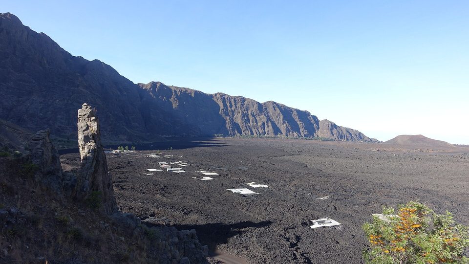 A dark lava field across a crater floor beneath a high curved wall