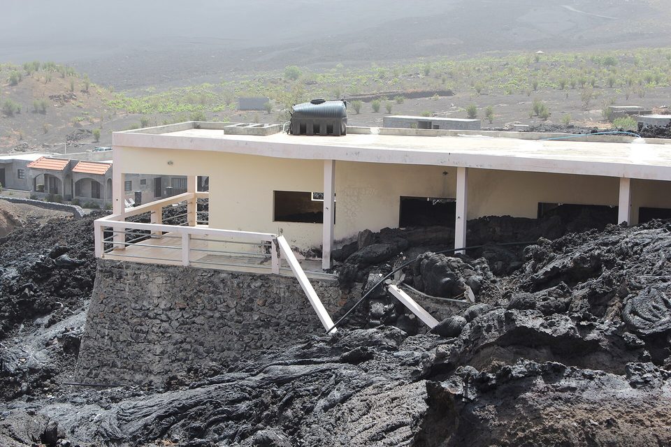 A building half swallowed by rough black lava up to its railing