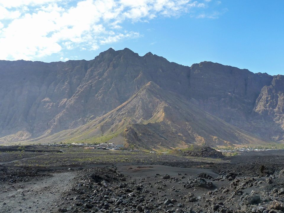 Two villages of pale houses strung along the foot of a high curved cliff on a black lava floor