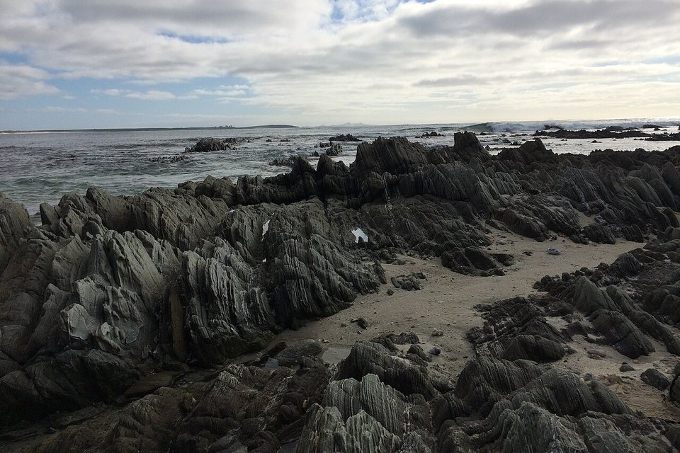 Grey fluted rock ribs with surf under a cloud-streaked sky
