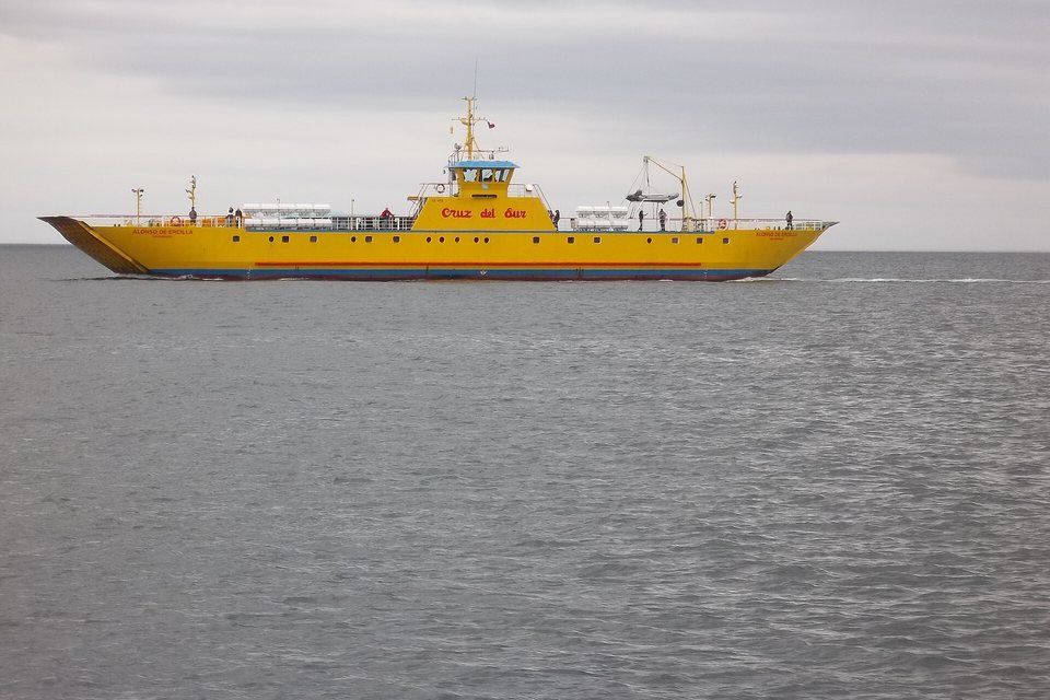 A long yellow car ferry crossing a grey channel under an overcast sky