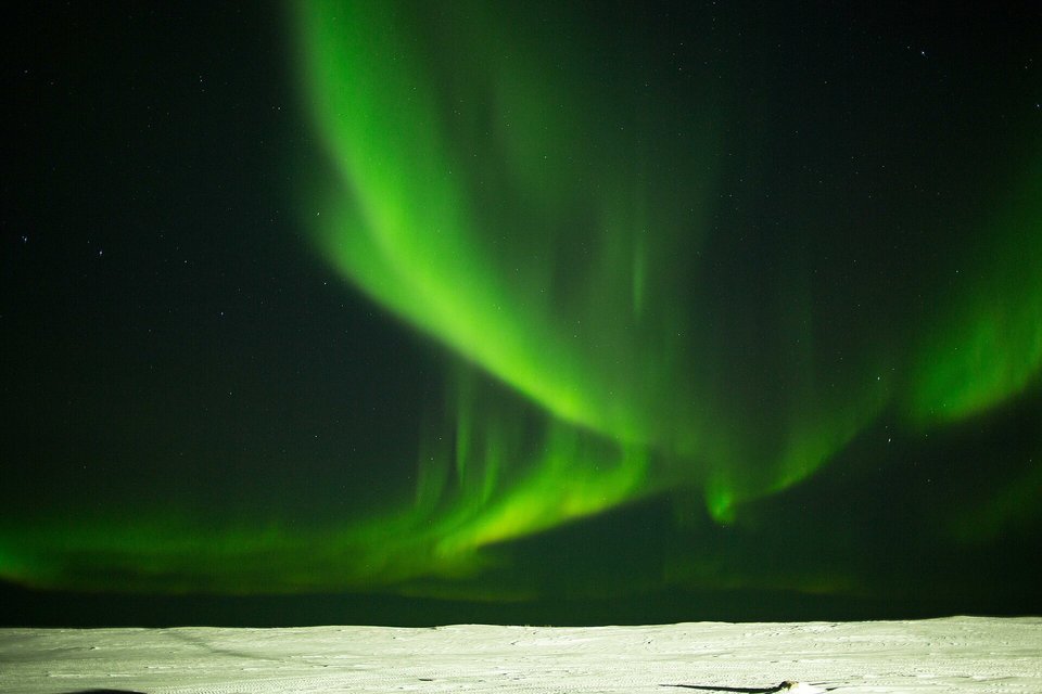 A sharp green aurora arching over a snow-covered foreground under a dark star-speckled sky