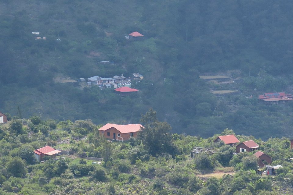 A scatter of small houses with red and grey roofs on a green forested slope deep inside a mountain valley