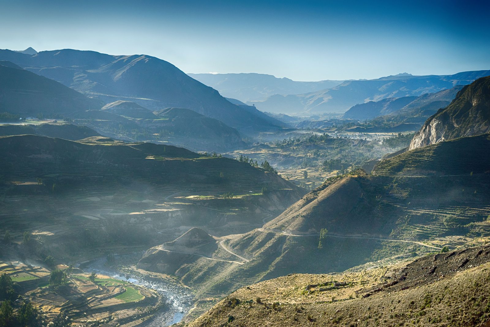 Morning haze lying in a deep valley, stepped terraces climbing the slopes, the river bright at the bottom and blue ridges going back to the horizon