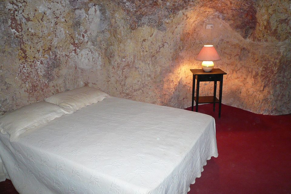 A bedroom cut into banded sandstone, a bed and a bedside table against the curved rock walls