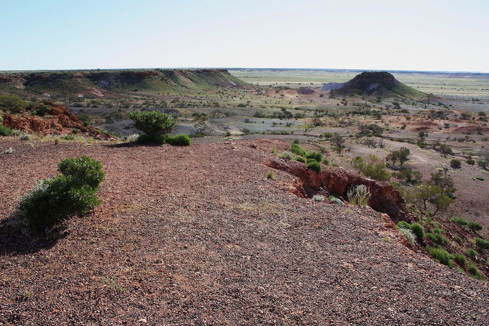 Flat-topped mesas and eroded hills in warm late light across red desert ground