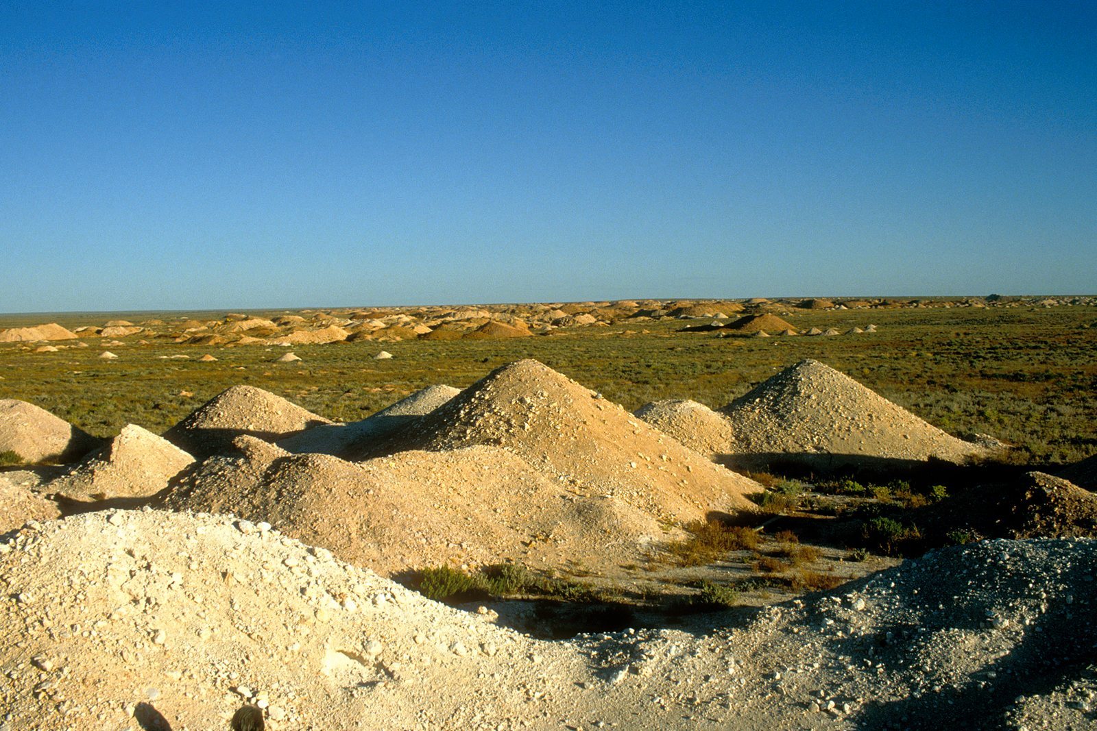 Conical heaps of pale mine tailings scattered across red desert ground under a clear blue sky