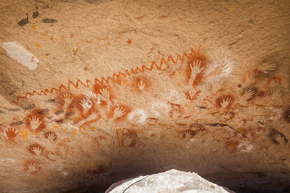 Red, white and black hand stencils with a zigzag line and an animal figure on rock