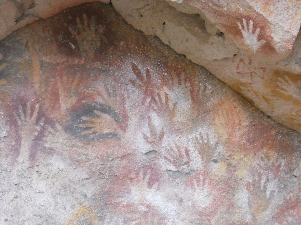 A dense wall of overlapping hand stencils in red, ochre and white