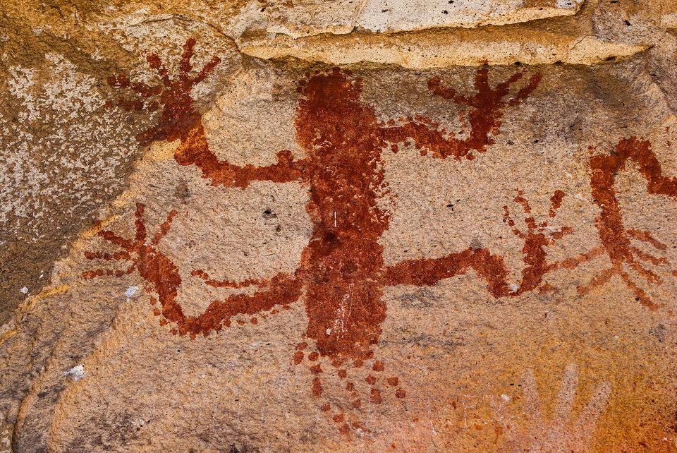 A red figure with outstretched limbs painted on rock among other marks