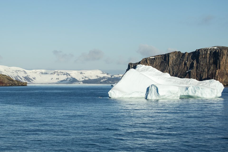 Calm blue water running through a gap between two dark cliffs toward open sea and distant snow-covered land