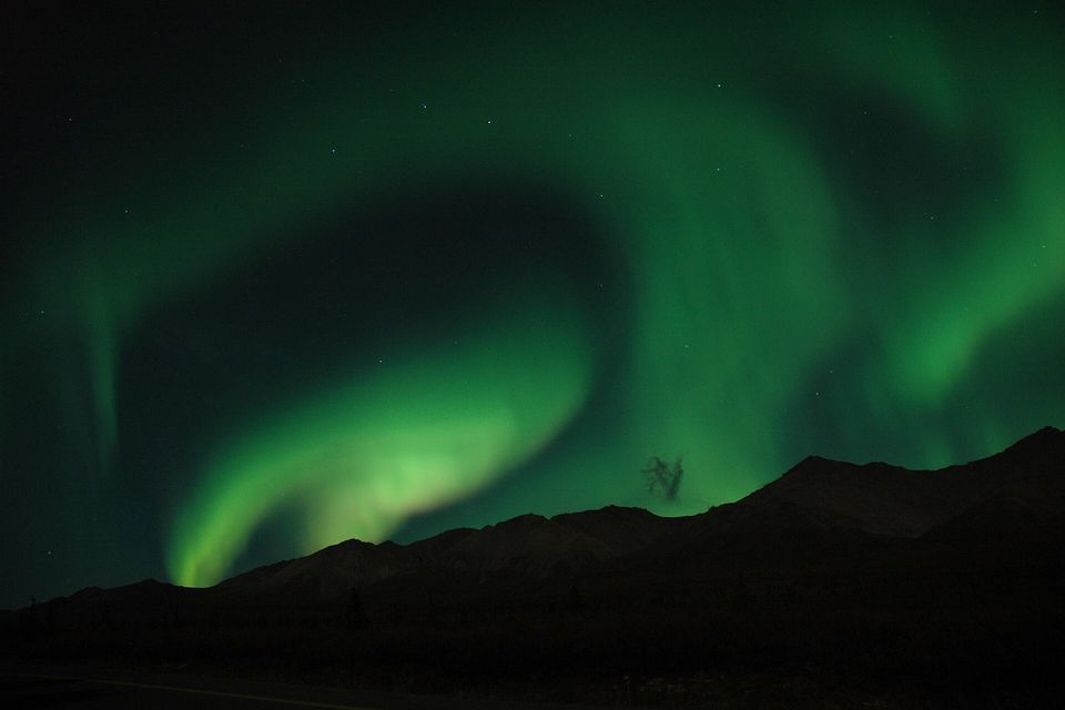 Green curtains of the northern lights over the dark outline of a mountain ridge