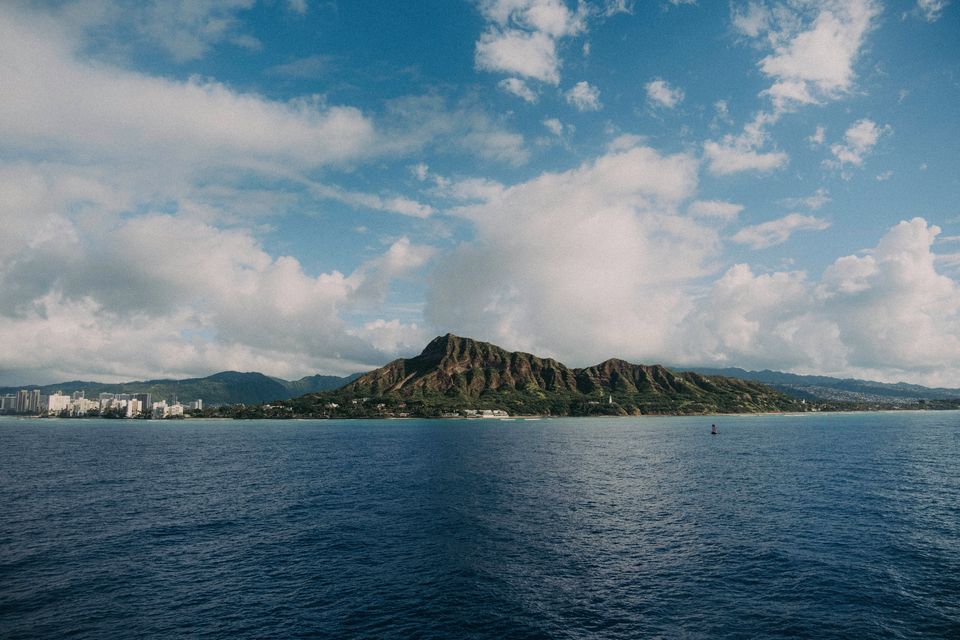 The long ridge of a volcanic crater over deep-blue water under cumulus clouds