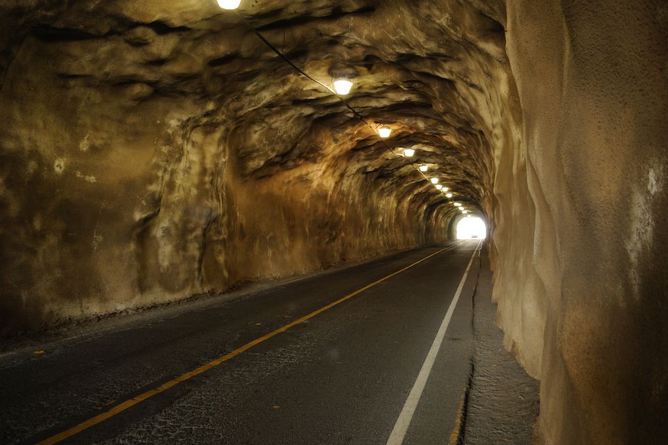 A lit road tunnel cut through a rock wall