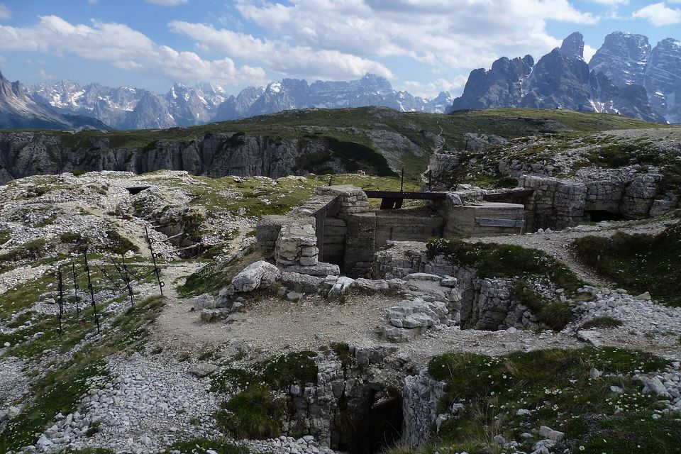 Stone-walled trenches and dugouts on a rocky summit with jagged peaks behind under a blue sky