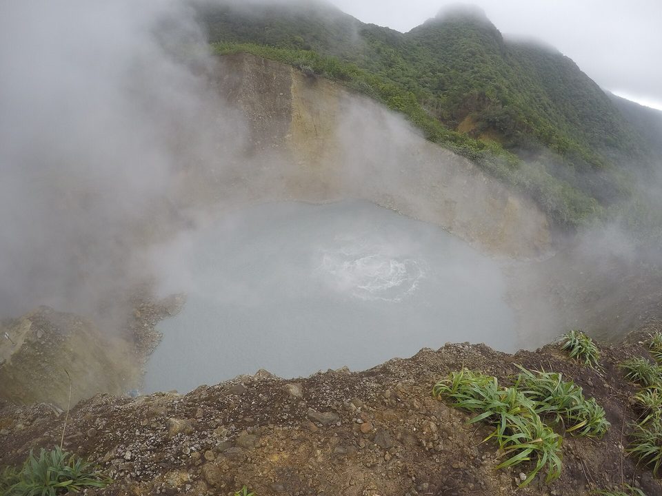 A grey lake giving off steam inside a green crater