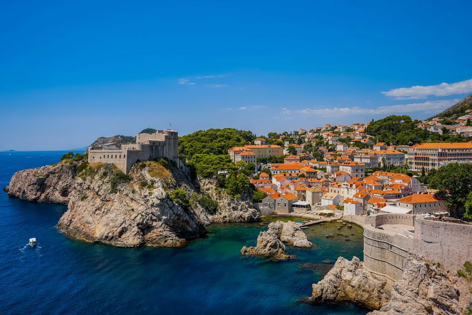 A stone fortress on a cliff above a small cove of clear water under a blue sky