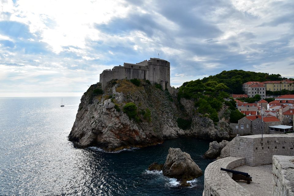 A fort high on a sea cliff above clear water under a big sky, a cannon on the wall in front