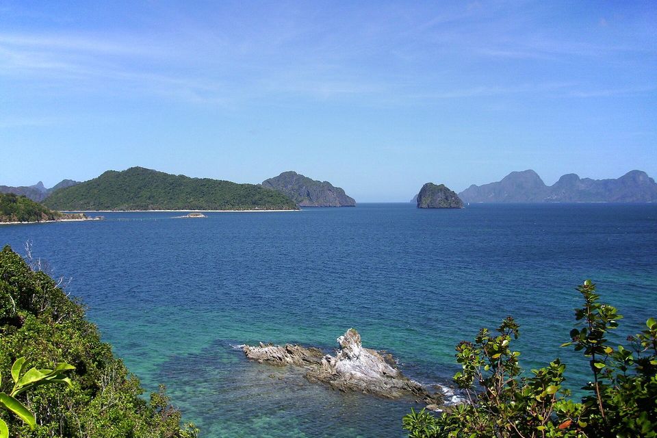The blue water of Bacuit Bay seen from a green hillside, with reef shallows below and islands along the horizon