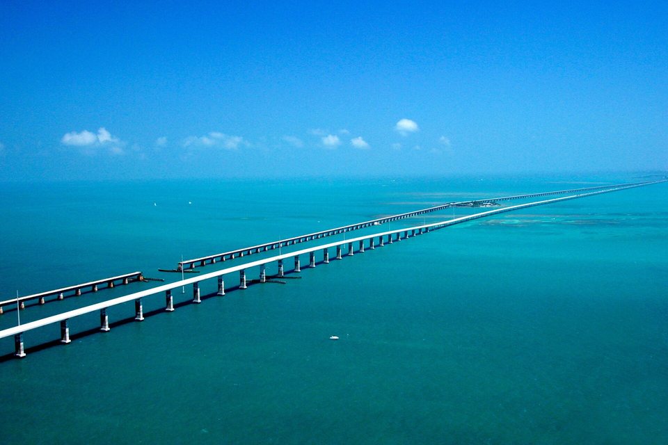 An aerial view of two long low bridges running parallel across turquoise sea to the horizon