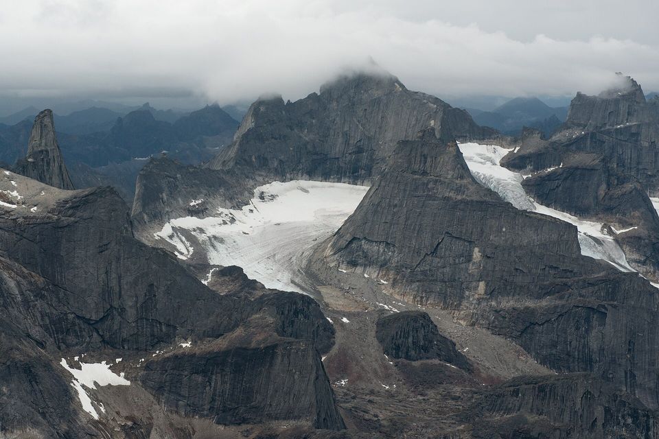 Jagged dark granite peaks with small glaciers between them, under low cloud