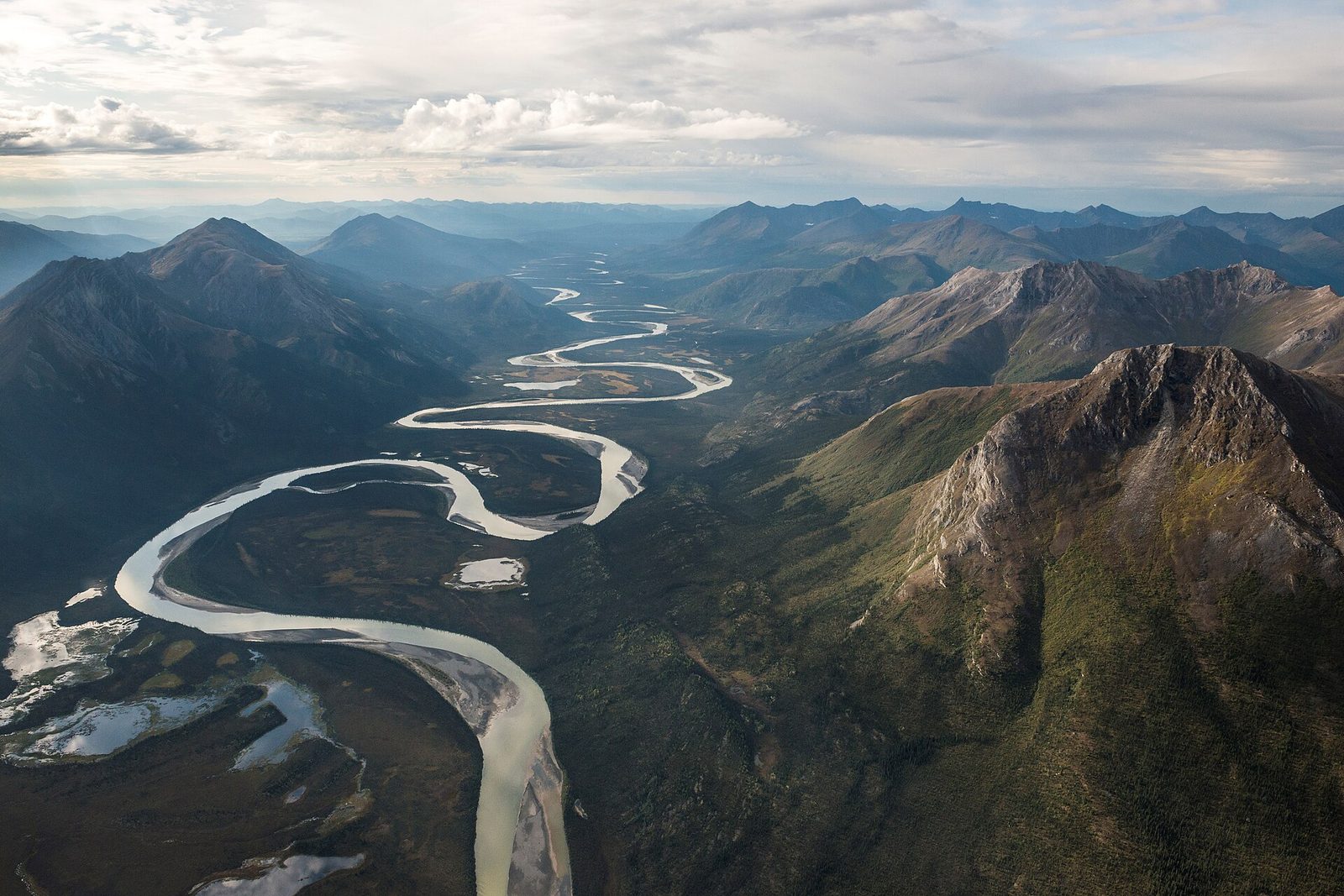 A river looping through a broad green valley between steep mountains, seen from the air, with no road or building in sight