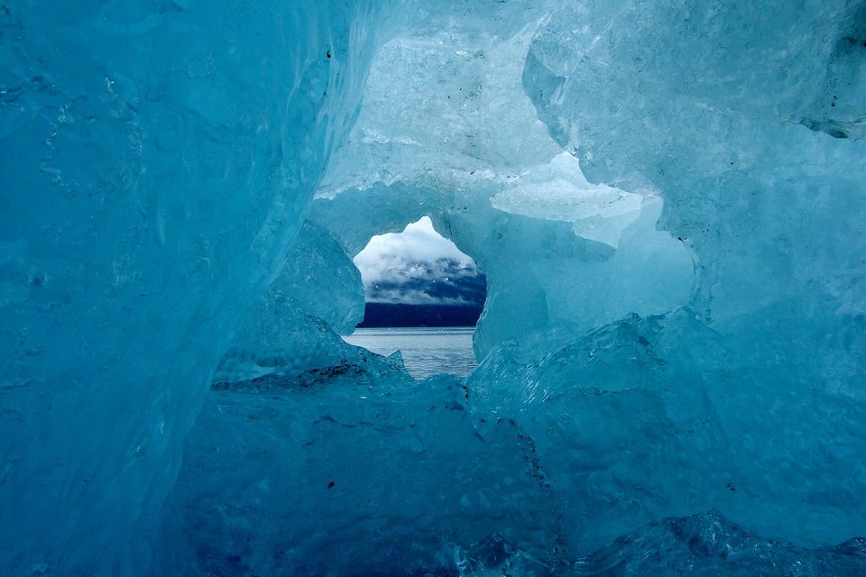 Translucent blue ice surrounding an opening that looks out over water to a mountain