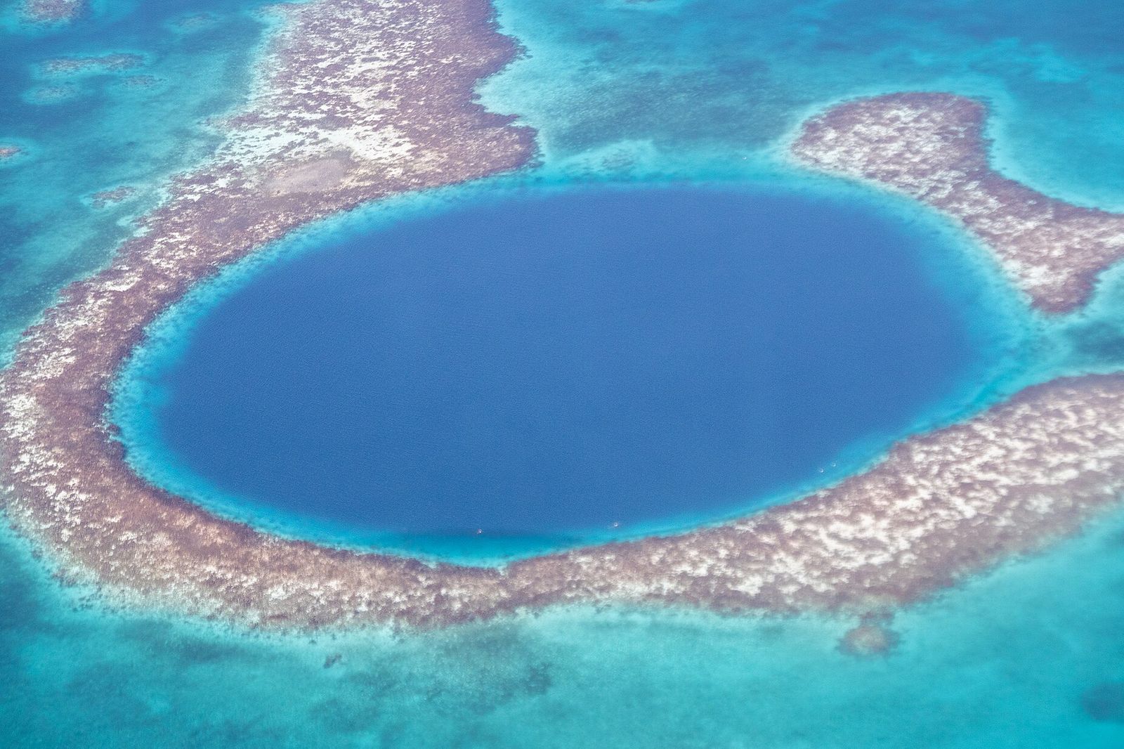 An aerial view of the Great Blue Hole: a perfectly round patch of deep navy water inside a pale reef ring, in shallow turquoise water