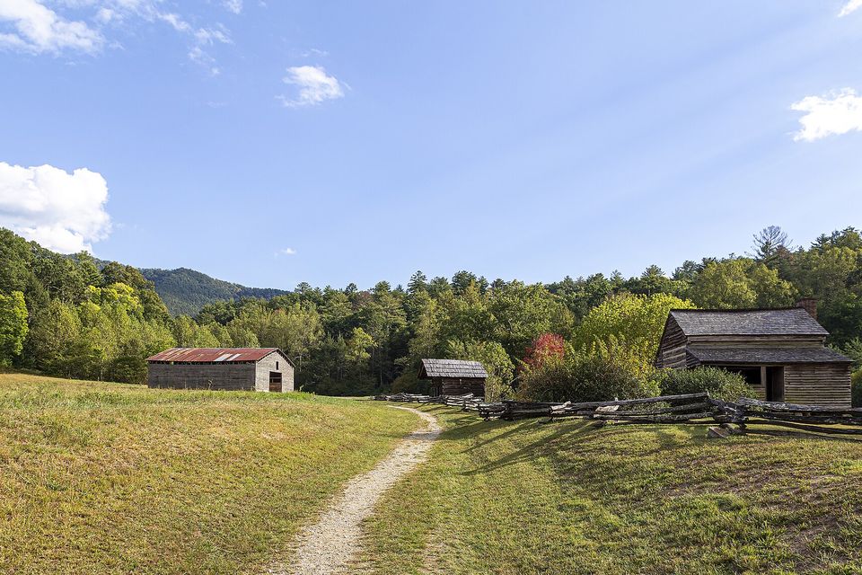 A log cabin and two outbuildings at the edge of an open grassy cove, a footpath leading toward them under a blue sky