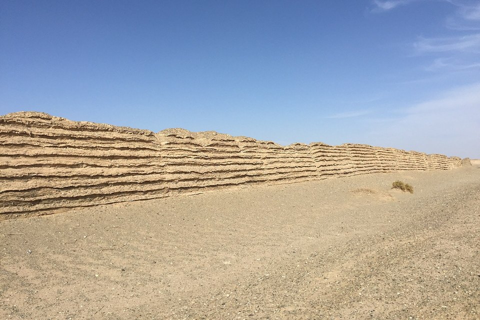 A long low wall of layered pale earth running across flat desert under a deep blue sky