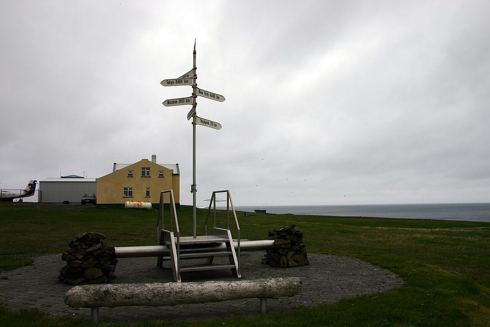 A signpost and bench on open ground marking the Arctic Circle on Grímsey