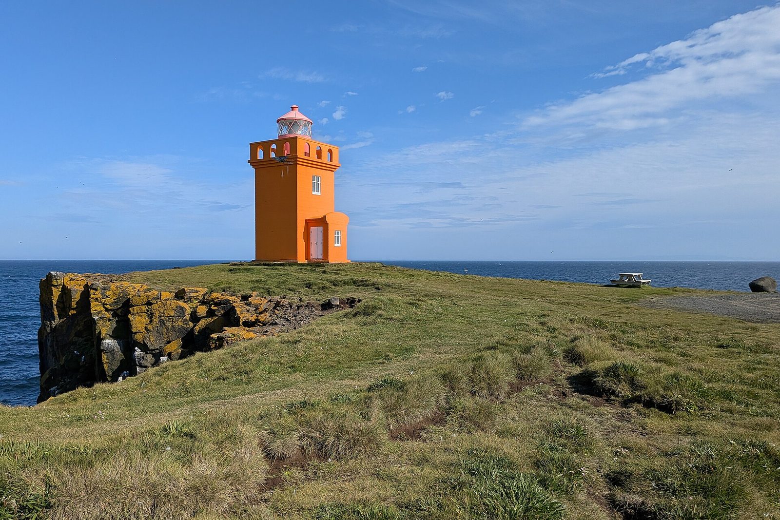 An orange lighthouse tower on dark basalt cliffs above a blue sea under a clear sky