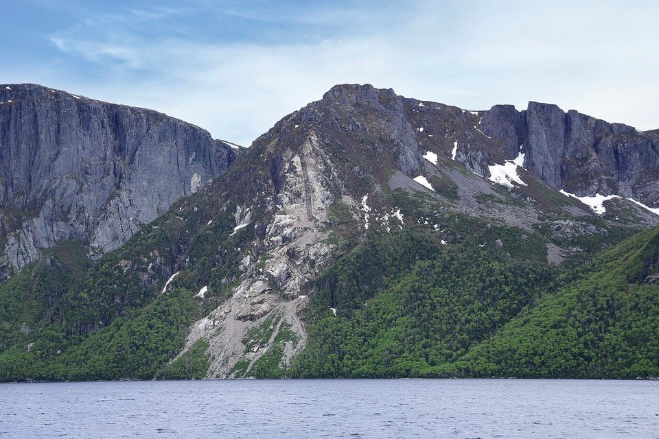 Grey rock cliffs and a forested slope with snow patches rising straight from a dark lake