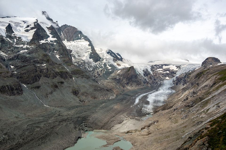 A dark snow-streaked summit above a long grey glacier tongue that ends in a milky green lake, bare moraine walls on either side
