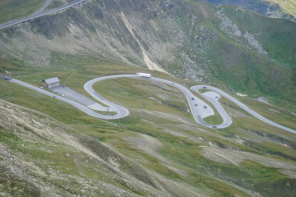 Tight loops of road laid out across a green-grey mountainside, a stone hut beside the lowest bend